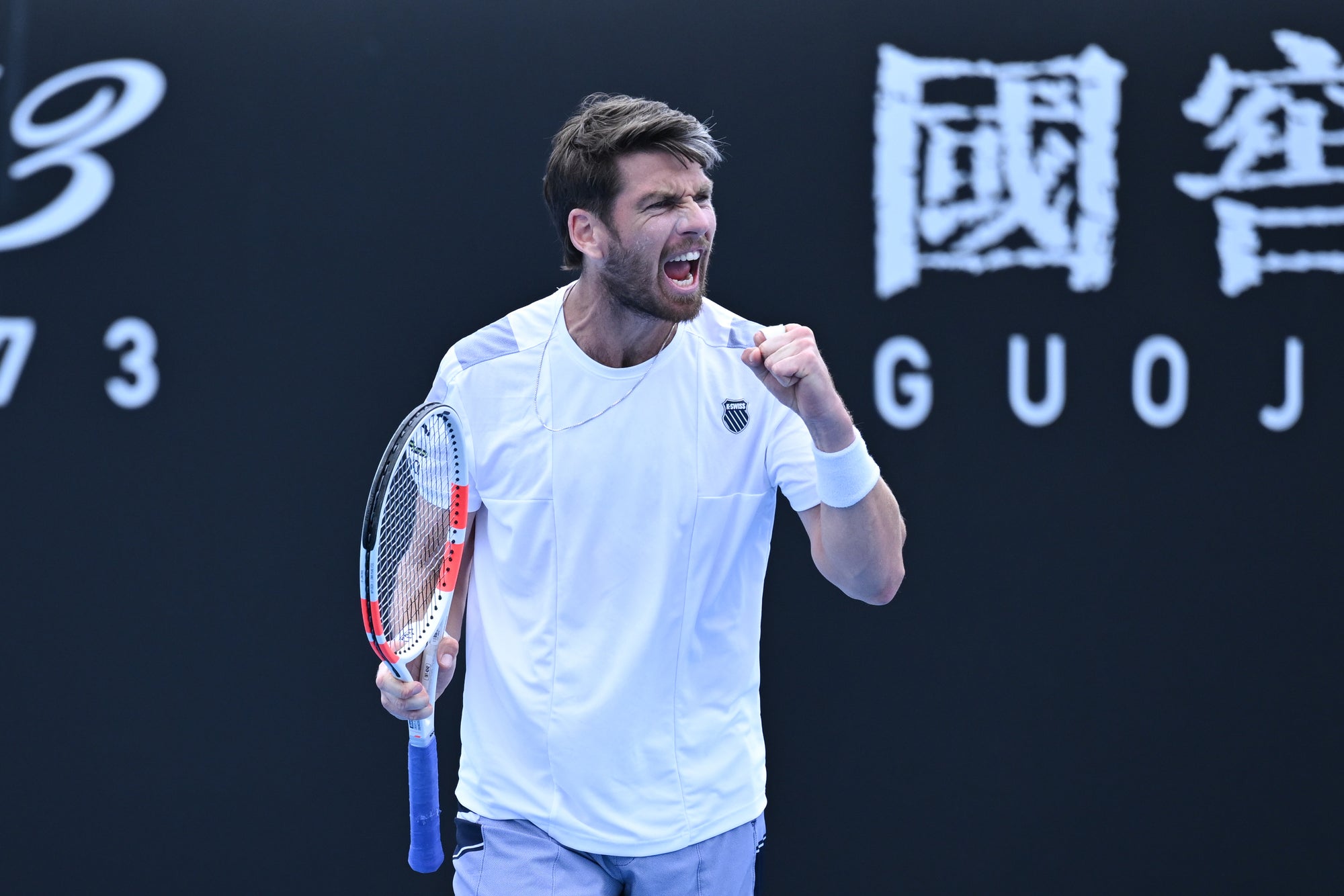 Cameron Norrie cheering on the tennis court, holding a tennis racket in his hand