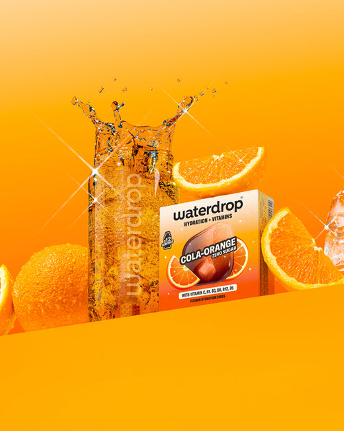 COLA ORANGE hydration cubes with vitamins beside sparkling water and oranges.