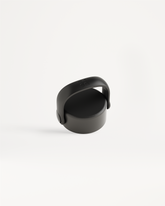 Carry Cap: Matte-black circular lid with a folding handle, featuring an embossed logo. Ideal for attaching bottles with a carabiner for easy transport.
