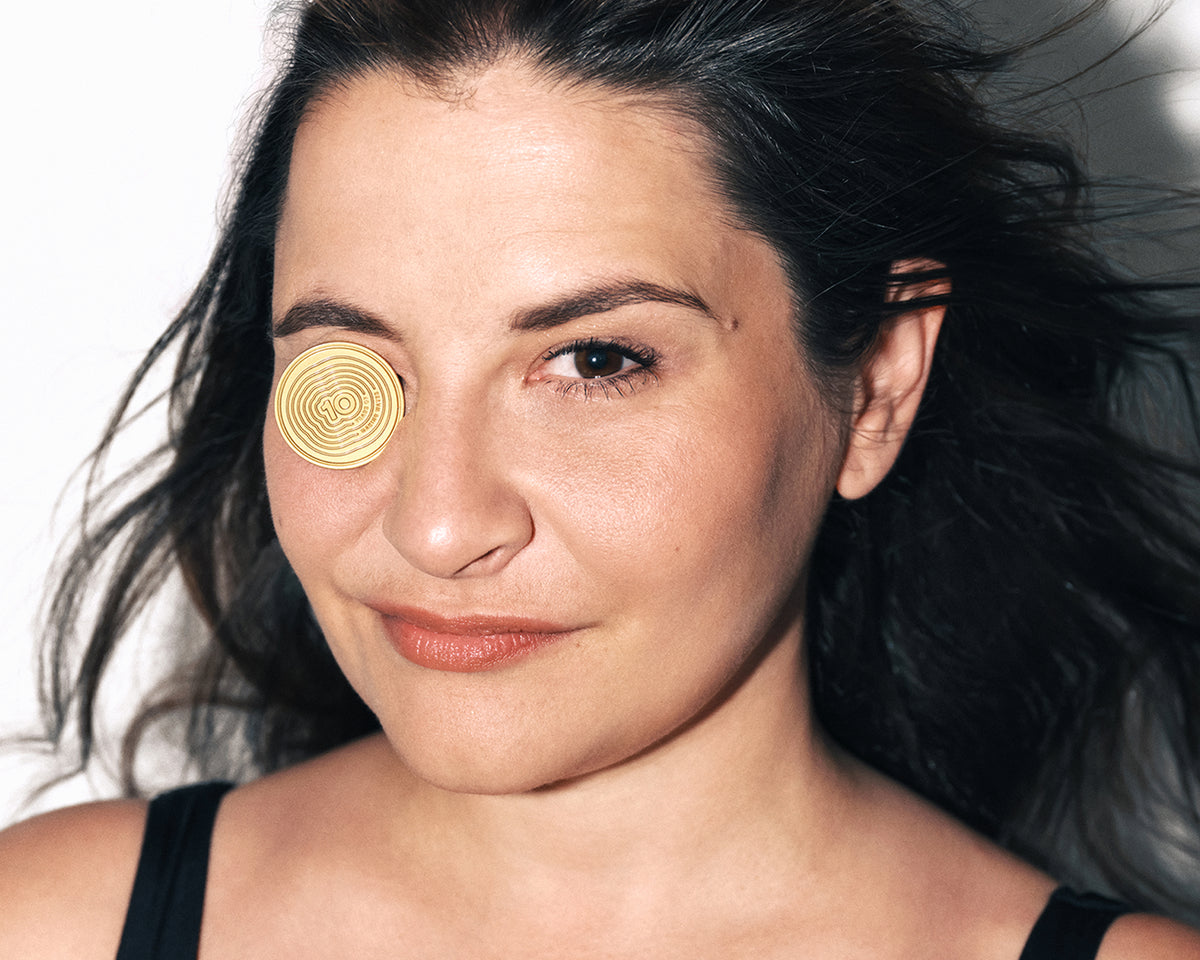 Close-up of a woman with a round gold cosmetic patch over one eye.