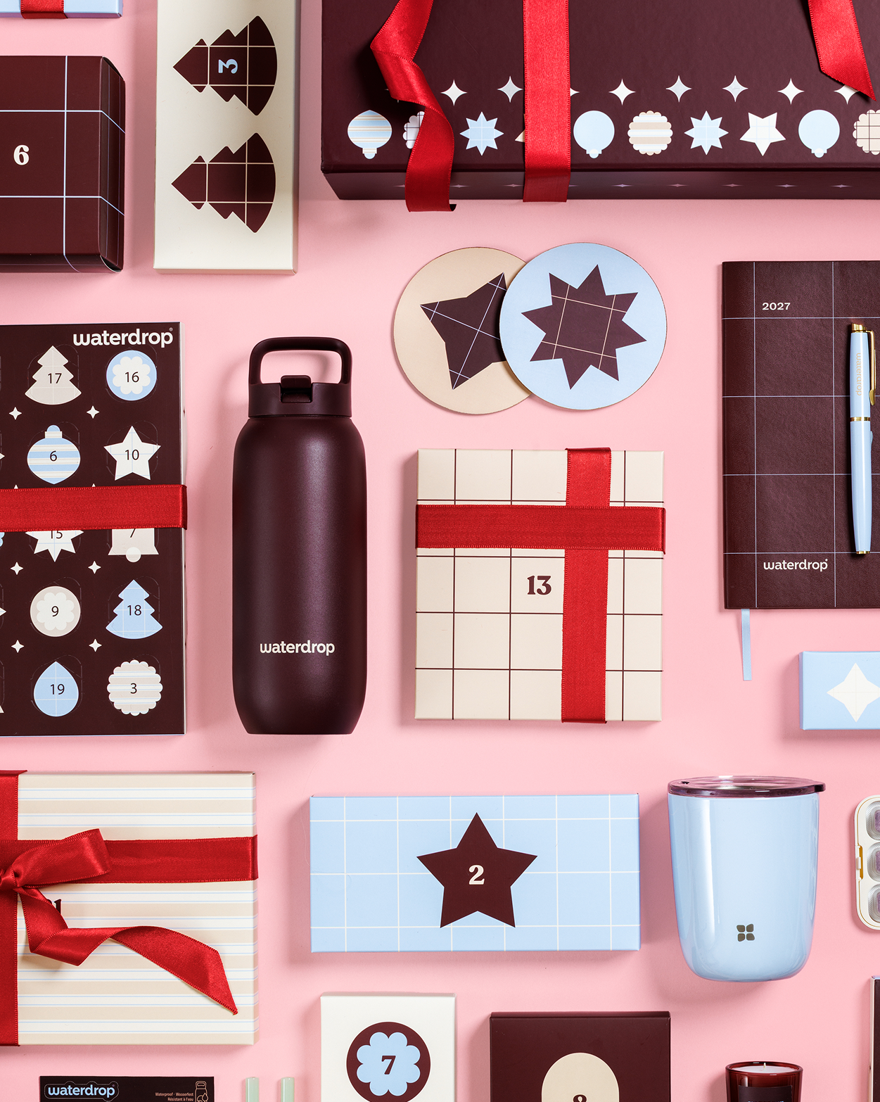 Assorted gift boxes, an advent calendar, a water bottle, a mug, and other wrapped presents arranged on a pink background.