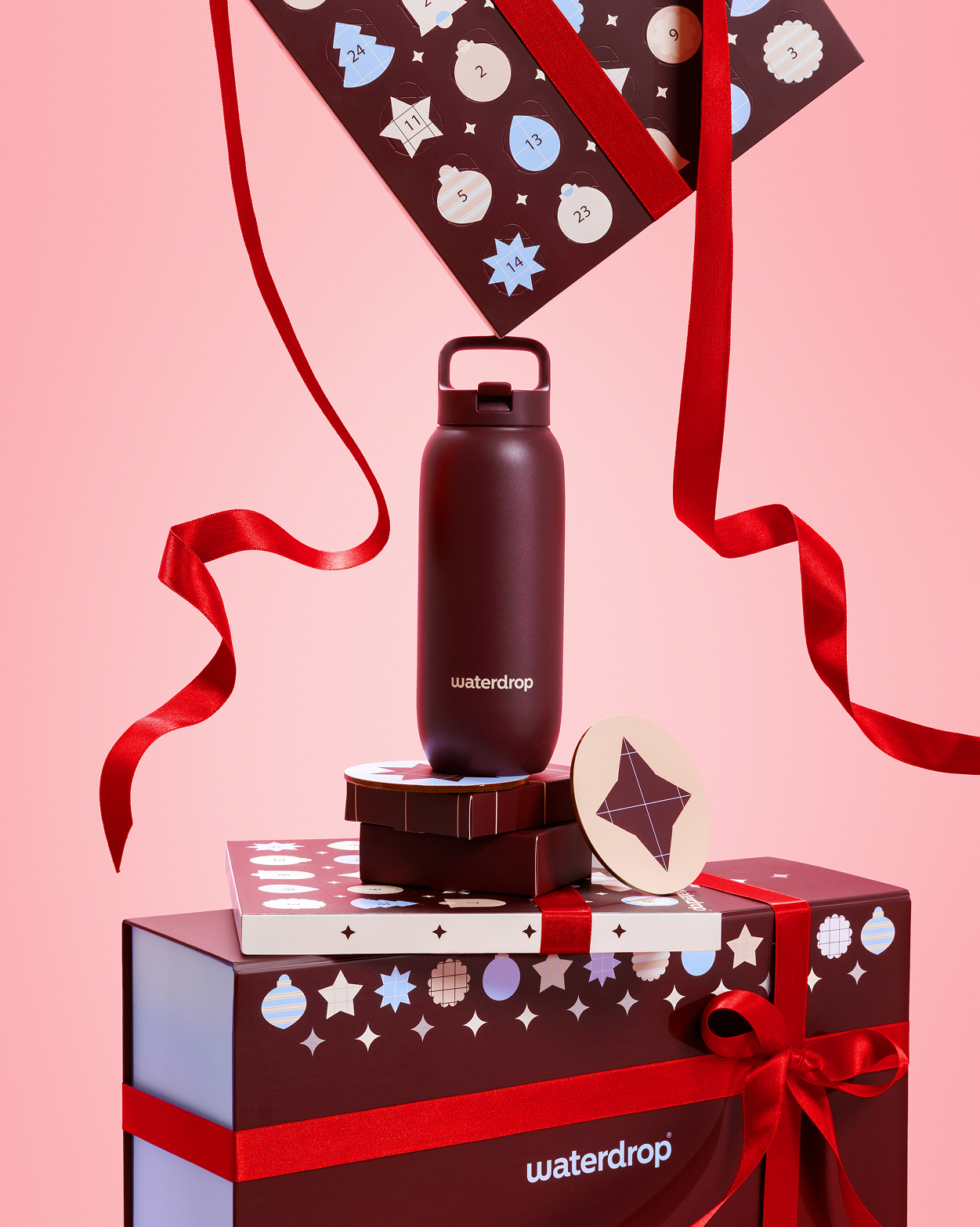 Dark bottle placed on gift boxes with red ribbons against a pink background.