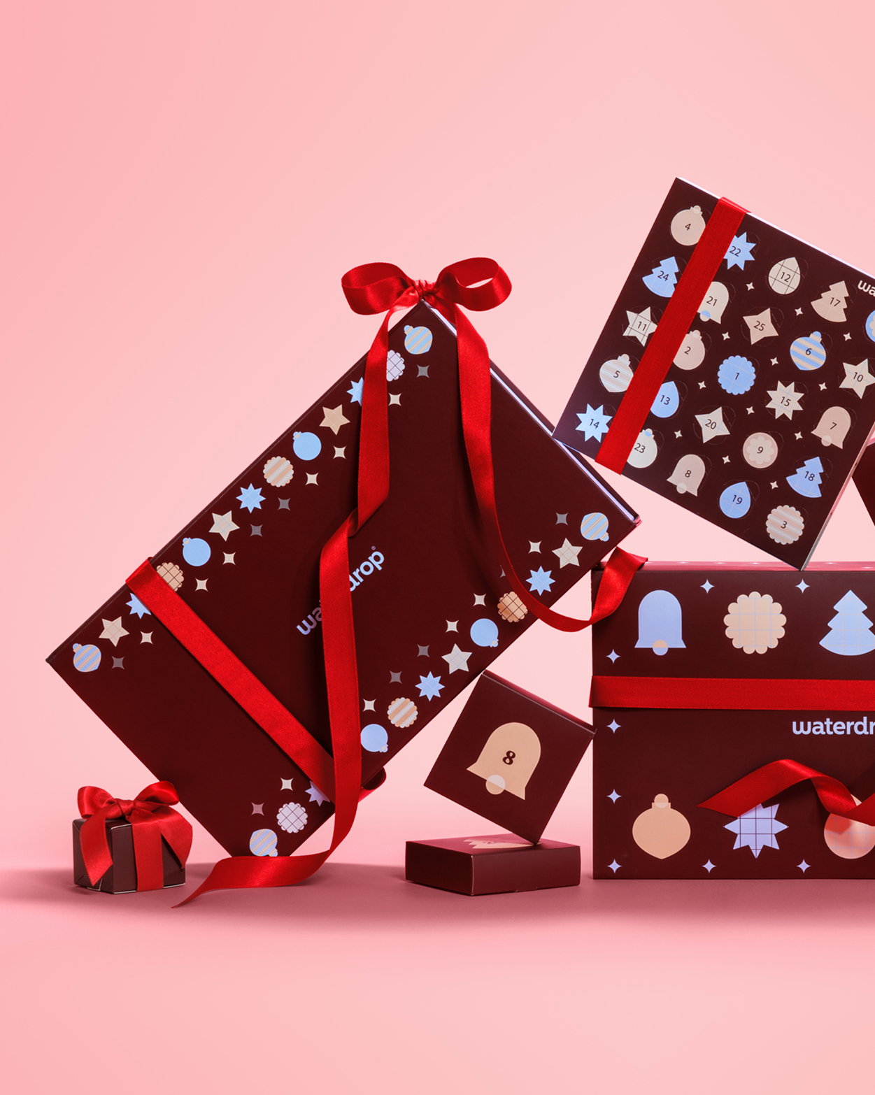 Wrapped gift boxes with red ribbons and festive patterns on a pink background.
