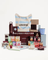 Assorted boxed products and containers arranged around a striped tote bag to form a gift set.