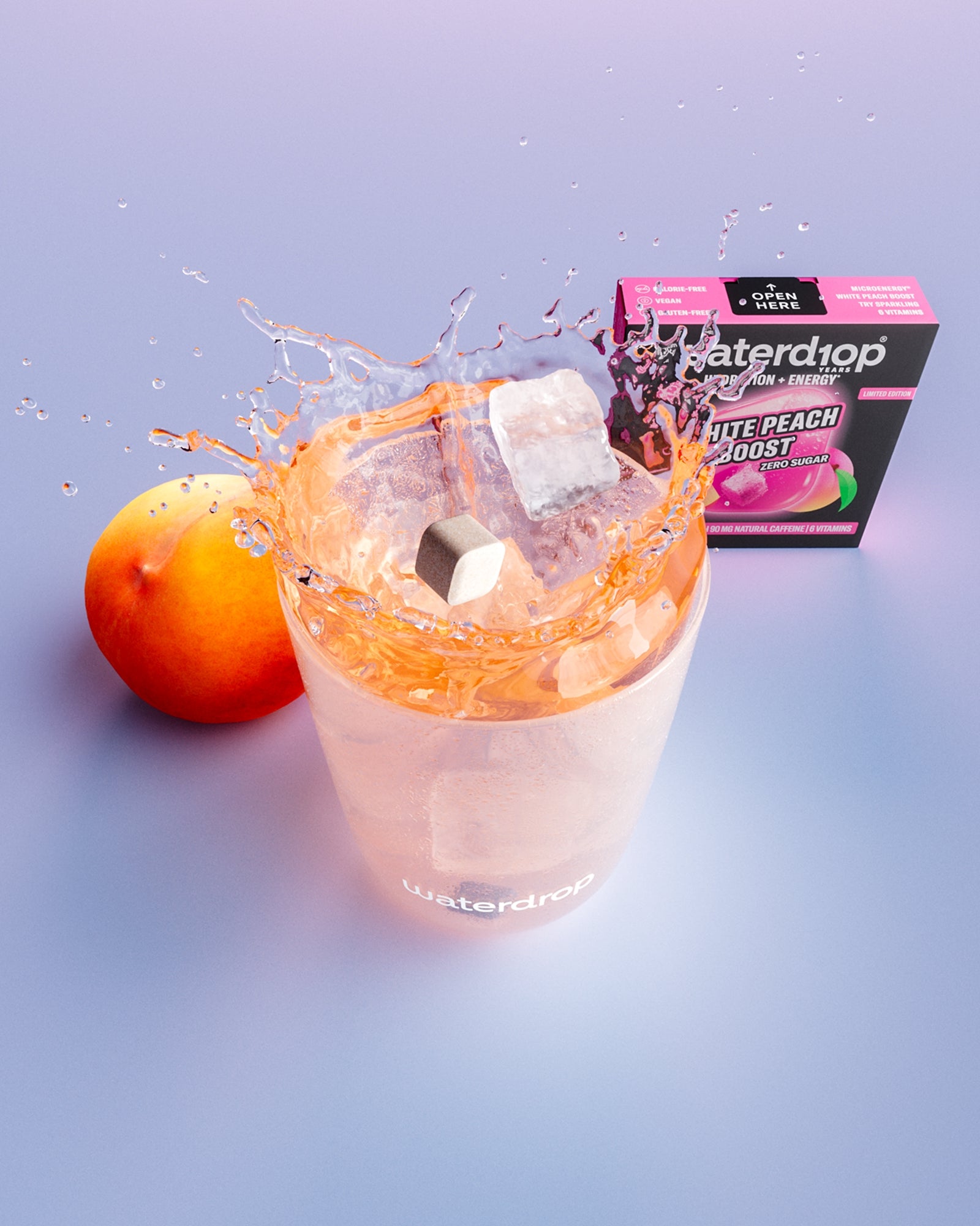 Glass with peach-flavored drink and ice cubes, a peach and a box in the background.