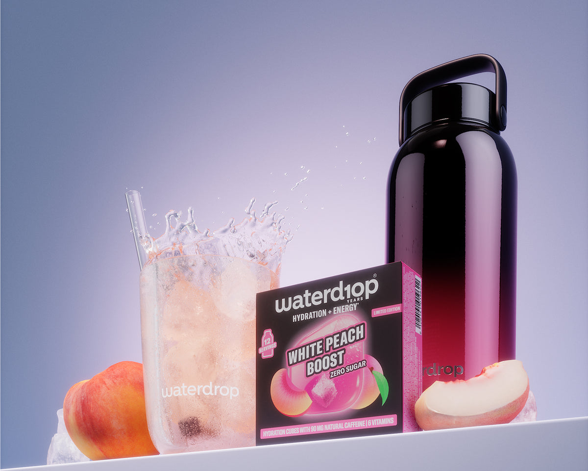 Box of White Peach Boost beside a glass of iced drink and a black reusable bottle on a white shelf.