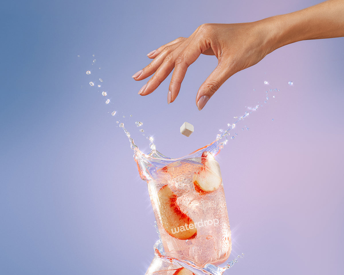 Hand drops a small ice cube into a glass of water with ice, creating a splash.