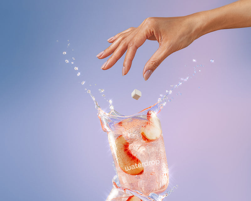 Hand drops a small ice cube into a glass of water with ice, creating a splash.