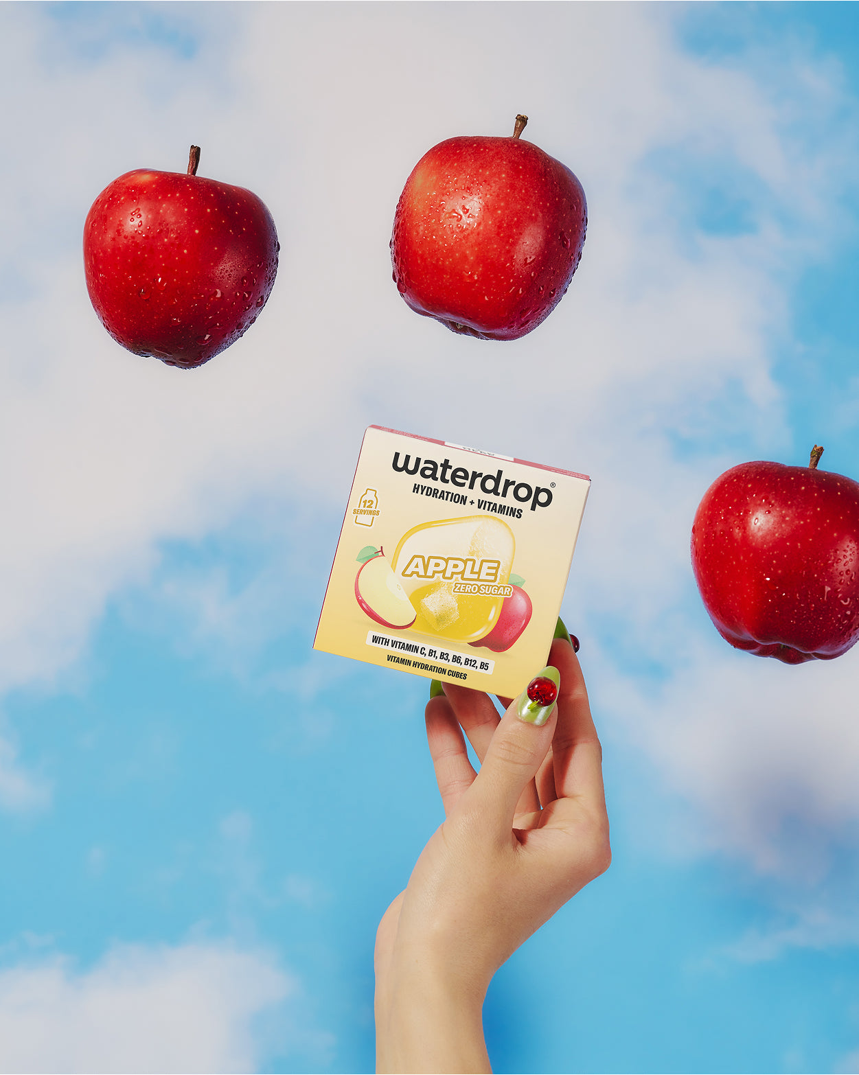 Hand holds a small fruit-product box as three red apples float against a blue sky