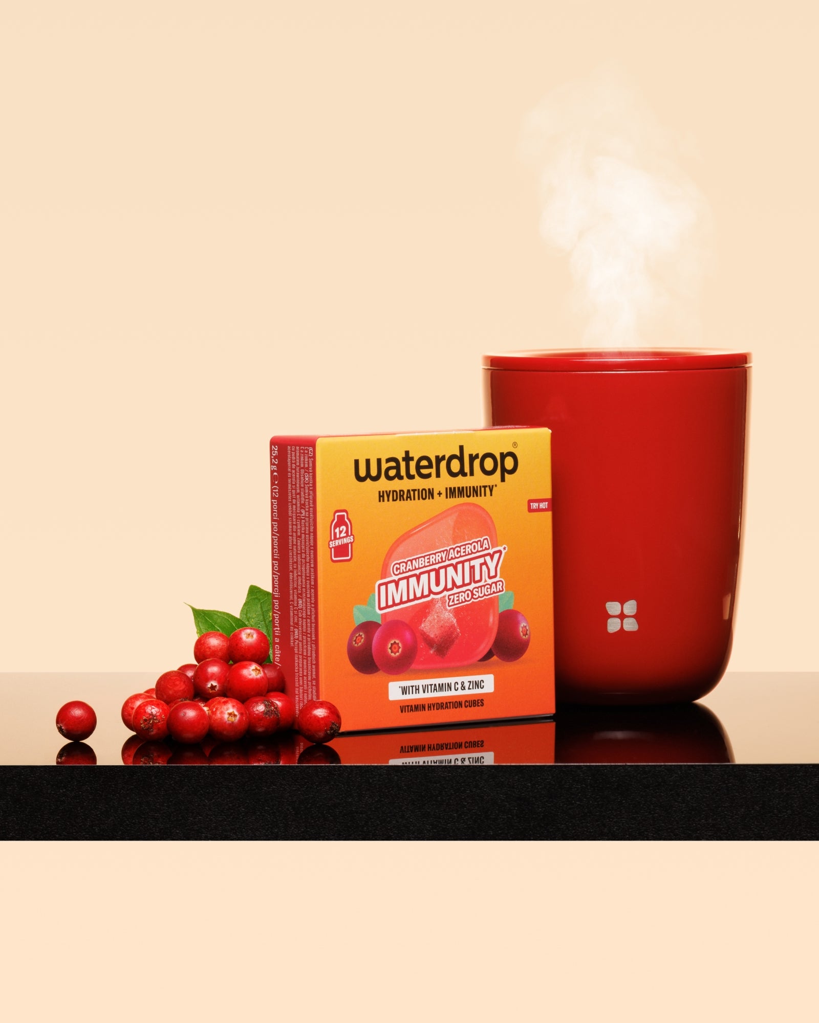 Red steaming mug beside a red-topped box and a cluster of cranberries on a glossy surface.