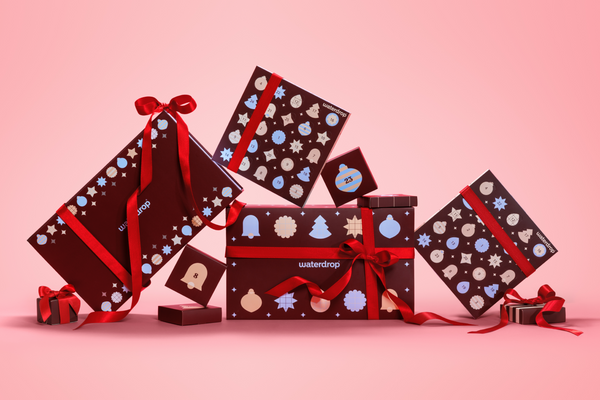 Assorted gift boxes wrapped in dark paper with red ribbons on a pink gradient background.