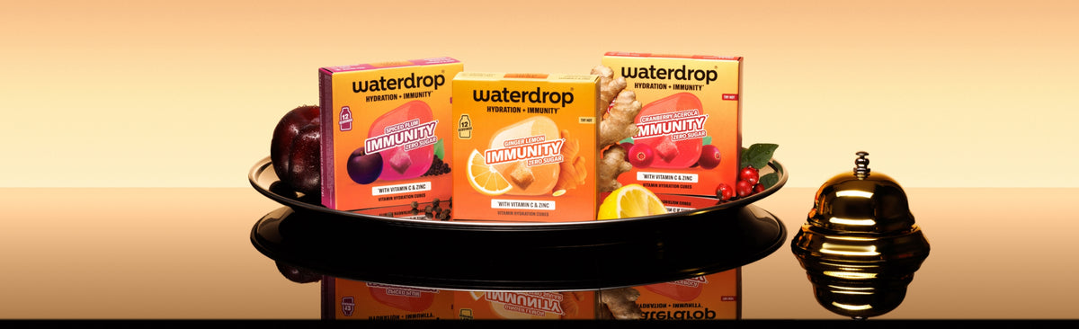 Tray with three Waterdrop product cartons on a reflective surface and a small decorative bottle on the right.