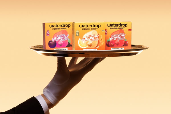 Gloved hand on a tray holding three small boxes against an orange background.