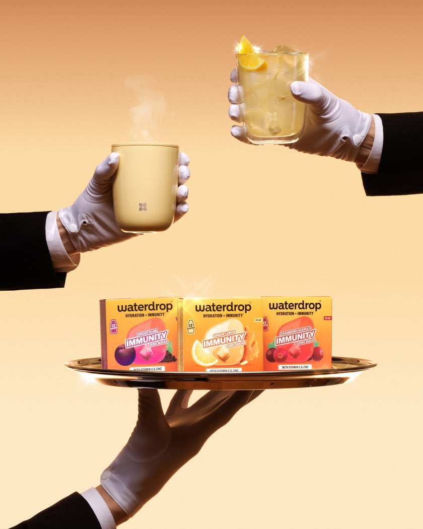 Tray carried by gloved hands presents three Waterdrop boxes and two cups, one with a lemon wedge.