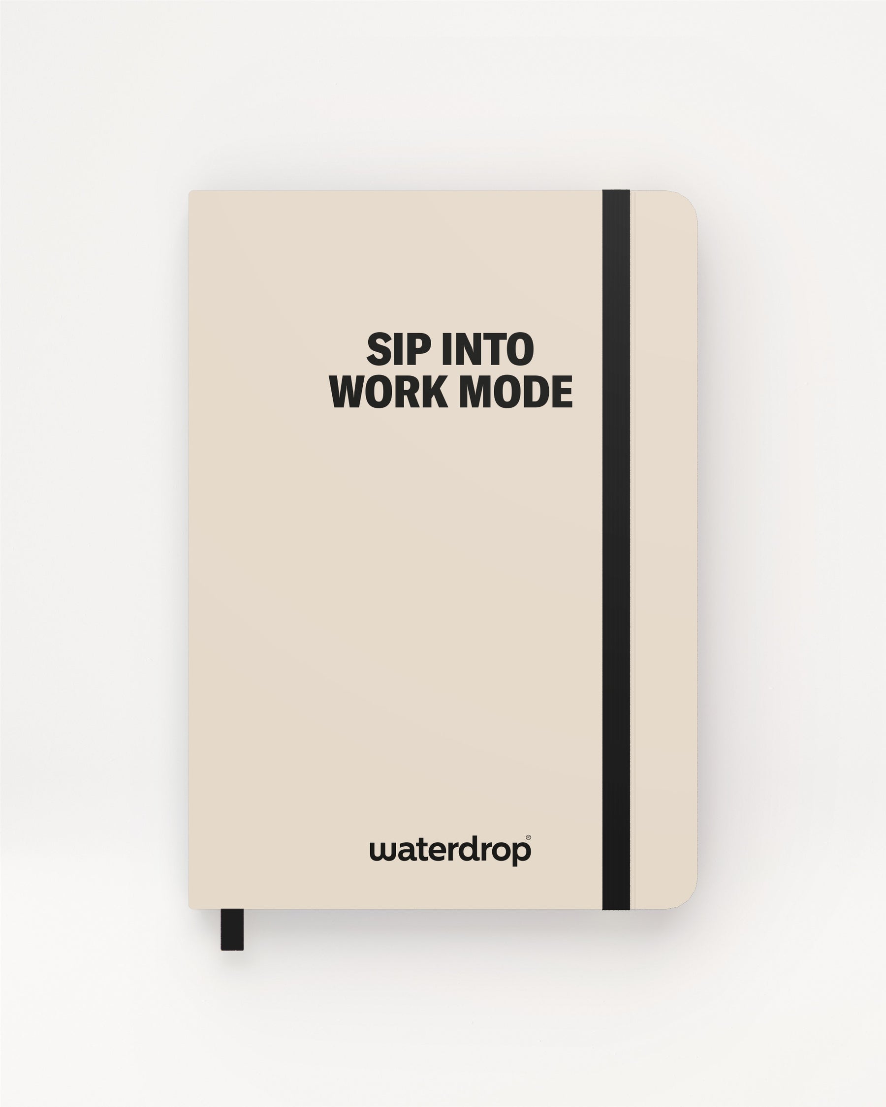 Beige hardcover notebook with a black elastic band and ribbon bookmark on a light background.